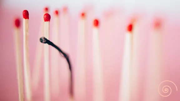 An image of standing matchsticks with one in the middle being burnt and black.