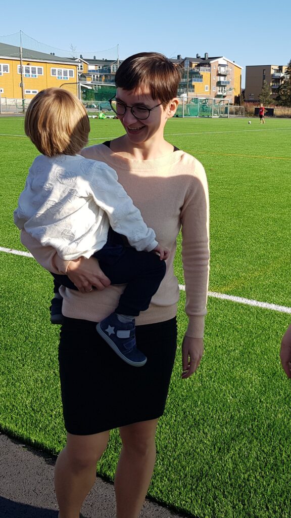 A picture of a woman with short hair and a black dress holding a child on her hip.